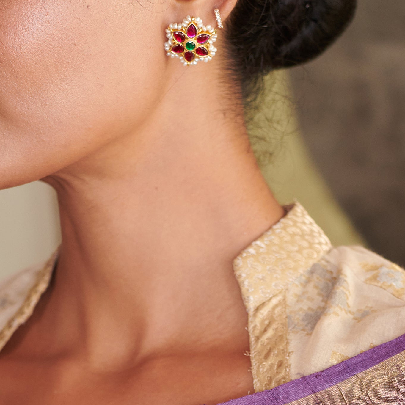 Close-up of a woman wearing a decorative earring with gemstones, dressed in a traditional outfit.
