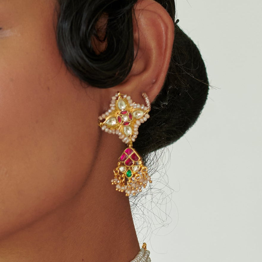Close-up of a person wearing a gold and gemstone earring on a plain background